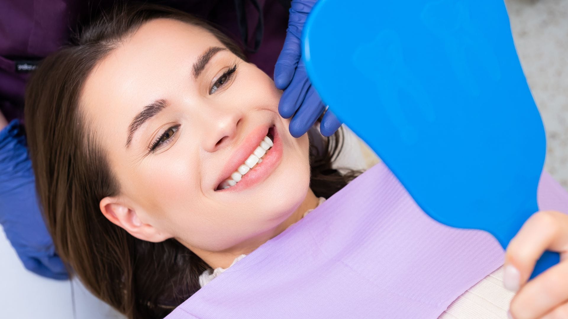 Woman looking in a mirror - teeth bonding vs veneers vs whitening.
