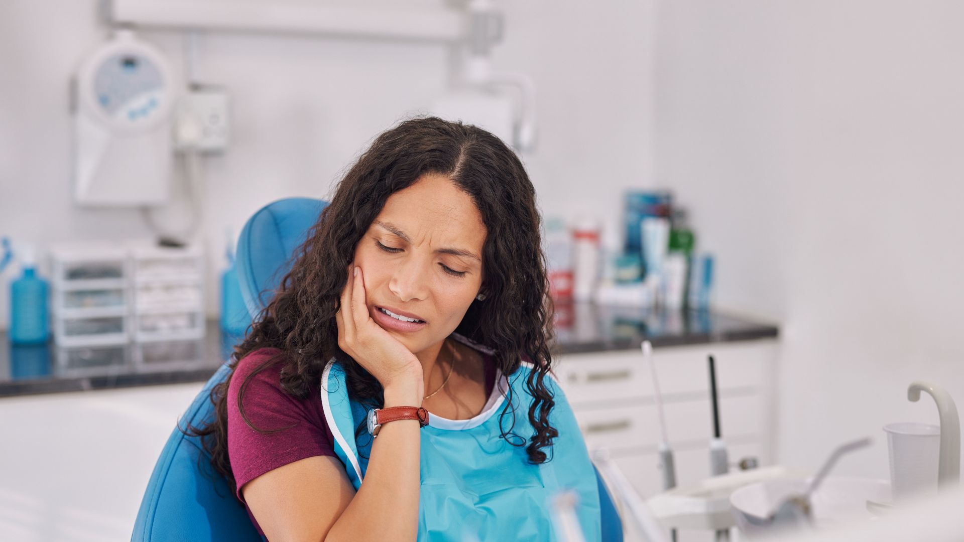 Woman holding her jaw in pain while at dentist's office - how to avoid bleeding gums - Midland Bay Dental. 